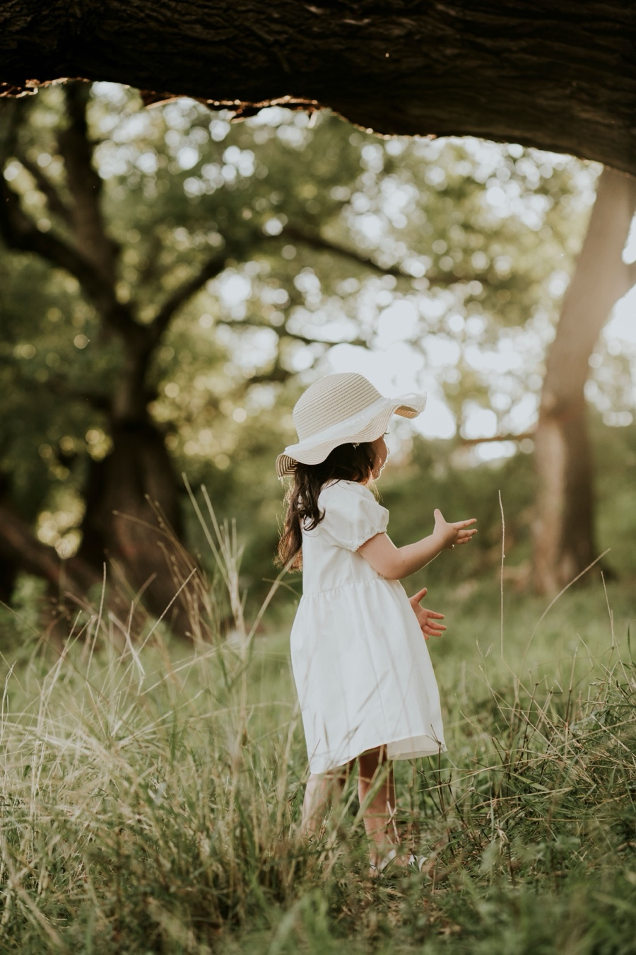 Petite fille en robe blanche et chapeau de paille dans les herbes hautes